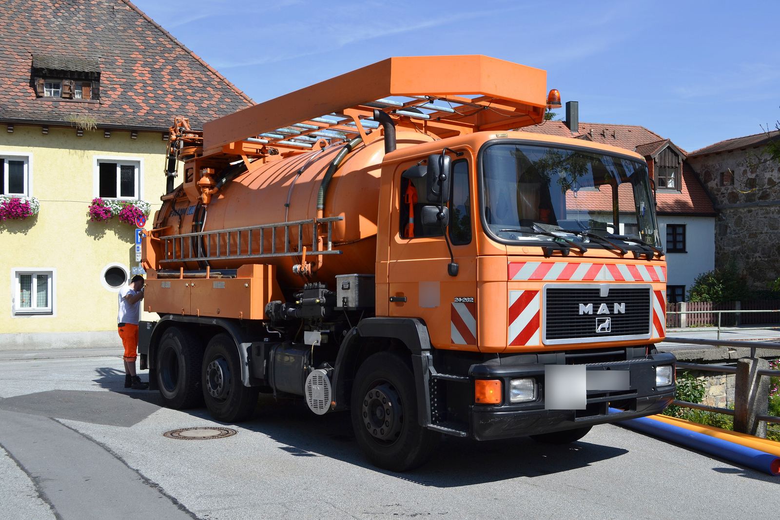 Autospecială de vidanjare portocalie parcată pe o stradă, pregătită de lucru